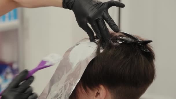 Profesionální kadeřnice žena barví dívky vlasy s barvením vlasů na fólii. — Stock video