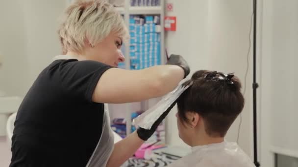 Professionele kapper vrouw verft meisjes haar met haarverf op folie. — Stockvideo