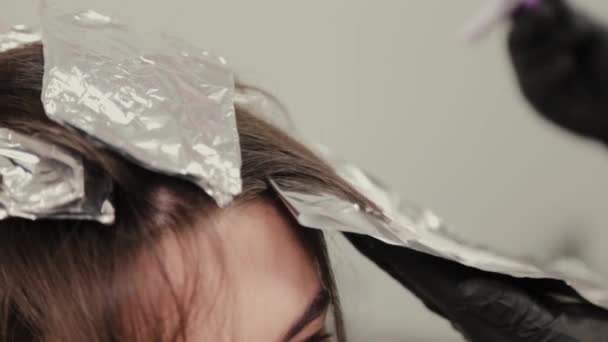 Професійна перукарня фарбує дівчаток волосся фарбою для волосся на фользі . — стокове відео