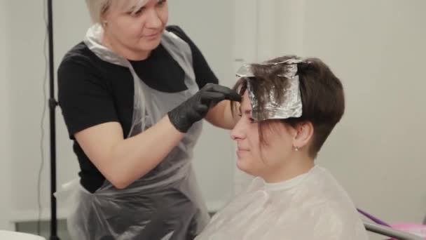 Professionele kapper vrouw verft meisjes haar met haarverf op folie. — Stockvideo