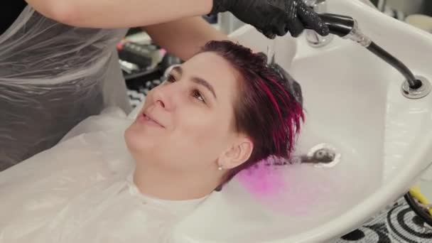 Επαγγελματική κομμώτρια γυναίκα πλένει τα μαλλιά βαφή στον πελάτη μετά τη βαφή. — Αρχείο Βίντεο