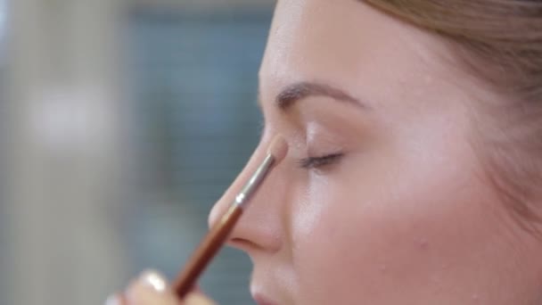 O artista de maquilagem profissional com uma escova aplica a sombra de olho a um cliente em um salão de beleza . — Vídeo de Stock
