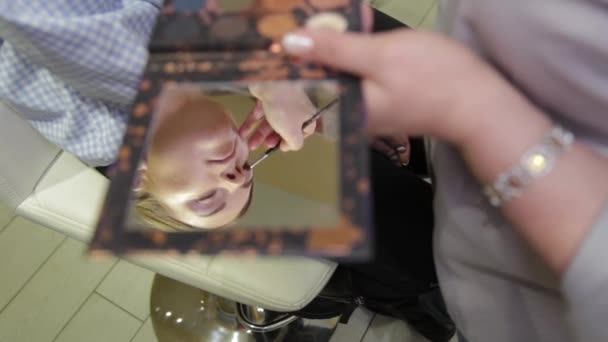 Professional make-up artist with a brush applies eye shadow to a client in a beauty salon. — 비디오