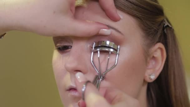 Make-up artist putting on make-up on models eyes with cosmetic equipment tool to twist eyelashes. Mascara Eyelash curler. — Stock Video