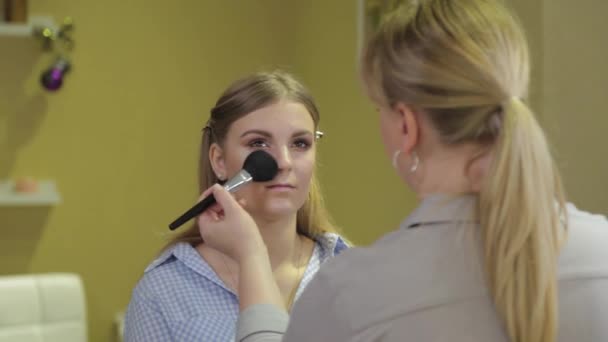 Professionelle Visagistin bürstet Puder auf das Gesicht der Kundin. — Stockvideo