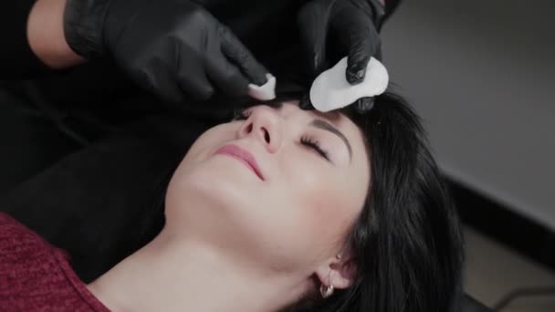 Professionele permanente make-up master verwijdert make-up van het gezicht met katoenen pads naar de klant. — Stockvideo