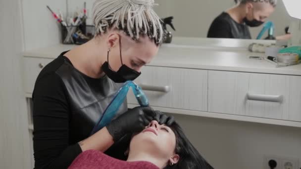 Um artista de maquiagem permanente profissional faz maquiagem permanente de sobrancelha com uma máquina de tatuagem . — Vídeo de Stock