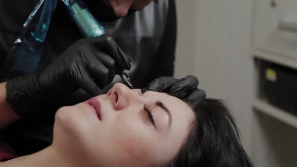 Un artista de maquillaje permanente profesional hace maquillaje de cejas permanente con una máquina de tatuaje . — Vídeos de Stock
