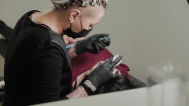 Ένας επαγγελματίας μόνιμος μακιγιέρ κάνει μόνιμο μακιγιάζ φρυδιών με ένα μηχάνημα τατουάζ. — Αρχείο Βίντεο