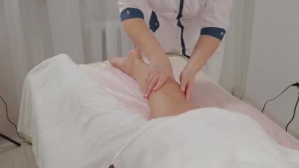 Mujer terapeuta de masaje hace masaje en los músculos de la pantorrilla de una niña . — Vídeos de Stock