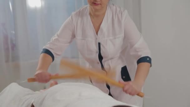 Vrouw massage therapeut doen massage met bamboe sticks naar een jong meisje. — Stockvideo