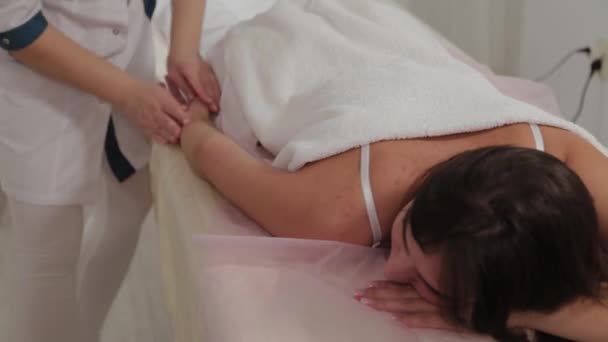 Mujer terapeuta de masaje haciendo masaje en todo el brazo a una chica joven en un salón de masajes . — Vídeos de Stock
