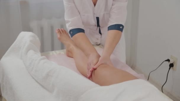 Γυναίκα θεραπεύτρια μασάζ κάνει μασάζ σε όλο το μήκος των ποδιών ενός νεαρού κοριτσιού. — Αρχείο Βίντεο