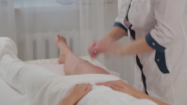 Γυναίκα θεραπεύτρια μασάζ κάνει μασάζ σε όλο το μήκος των ποδιών ενός νεαρού κοριτσιού. — Αρχείο Βίντεο