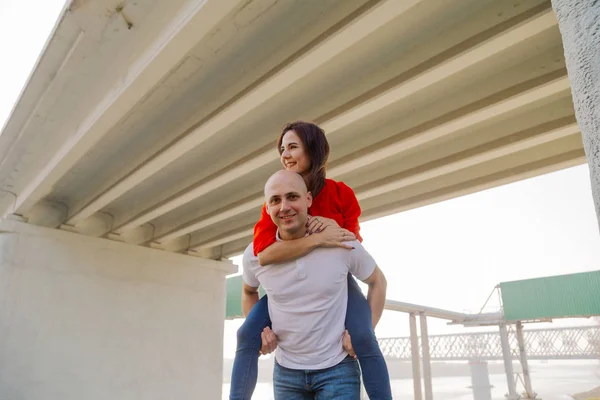 Bonne fille sur le dos d'un homme au pont. Les amoureux s'amusent . — Photo