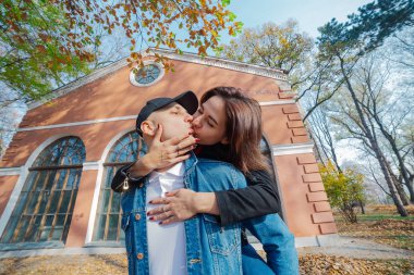 Genç ve güzel bir çift ve parktaki labradorları. Bir adam bir kadını sırtında tutuyor ve kadın ona sarılıyor. Batan güneş ışınları ağaçların dallarını delip geçiyor. Dikey çerçevelenmiş çekim..