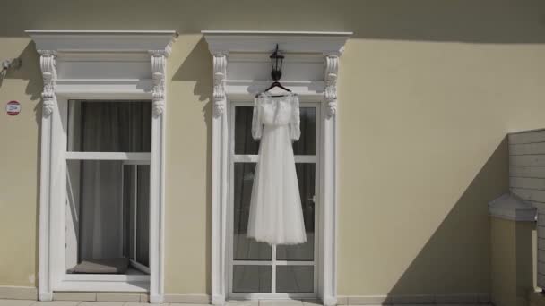 Beautiful modern wedding dress hanging in the house by the window. — Stock Video