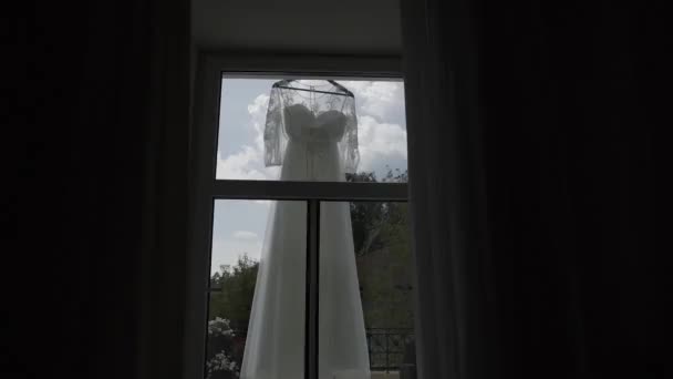 Beautiful modern wedding dress hanging in the house by the window. — Stock Video