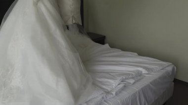 Mutlu gelin, odadayken gelinliğini elinde tutuyor..