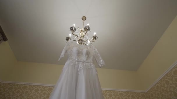 White wedding dress hanging on a chandelier in a room. — Stock Video