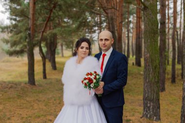 Mutlu gelin ve damat sonbahar ormanında el ele tutuşuyorlar..