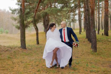 Mutlu gelin ve damat sonbaharda el ele tutuşarak ormanda yürürler..