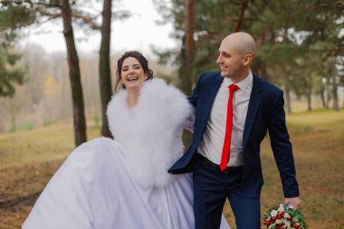 Mutlu gelin ve damat sonbaharda el ele tutuşarak ormanda yürürler..