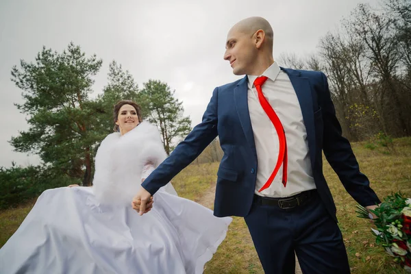 Novia y novio felices caminan por el bosque en otoño tomados de la mano . — Foto de Stock