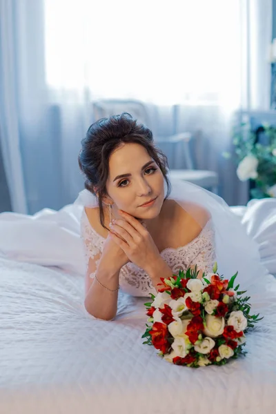 Hermosa novia feliz en la cama con un ramo de bodas . —  Fotos de Stock