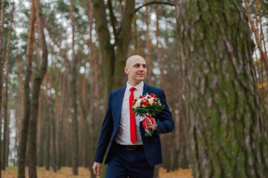 Sonbahar ormanında buketi olan mutlu bir damat..