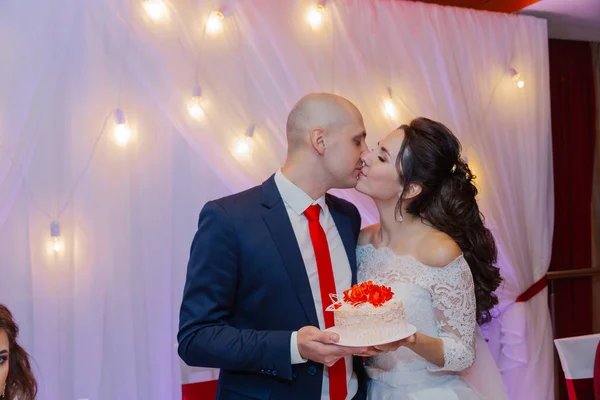 Heureux jeunes mariés tiennent un gâteau de mariage dans leurs mains . — Photo