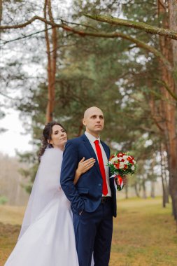 Mutlu gelin ve damat sonbahar ormanında el ele tutuşuyorlar..