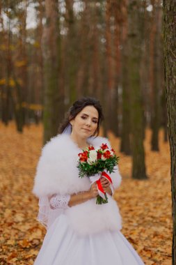 Beautiful happy bride with a wedding bouquet in the forest in autumn.