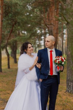 Mutlu gelin ve damat sonbahar ormanında el ele tutuşuyorlar..