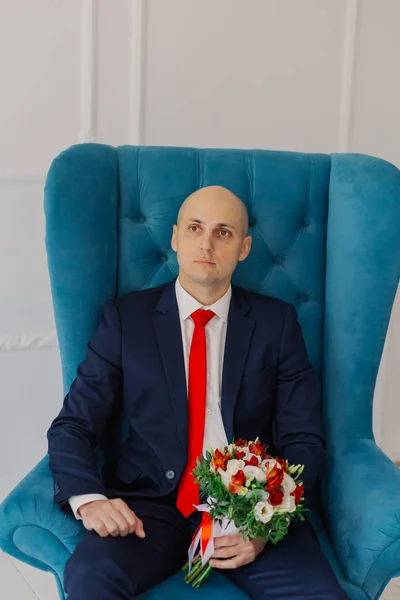 Jóképű vőlegény ül egy széken esküvői csokorral. — Stock Fotó
