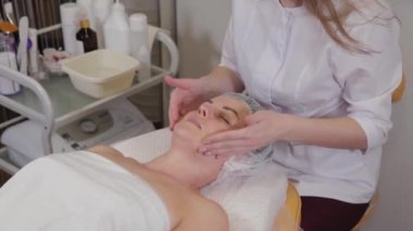 Profesyonel güzellik uzmanı kadın hastaya yüz masajı yapıyor..