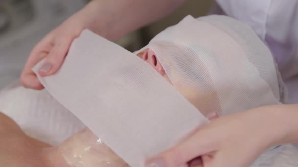 Профессиональная косметолог покрывает маску бинтами для лица . — стоковое видео