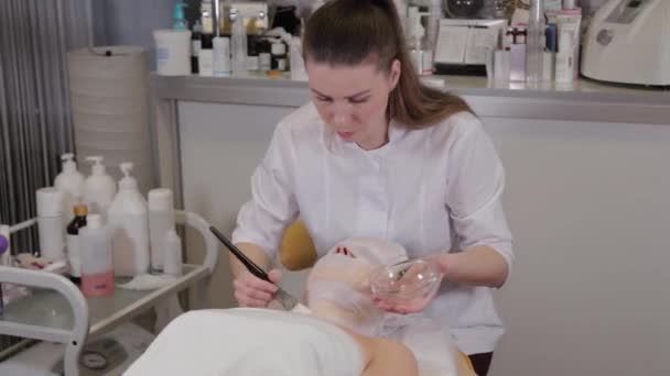 Cosmétologue professionnelle femme appliquant une solution tonique avec une brosse sur les bandages sur le visage des clients . — Video