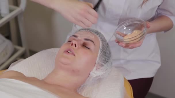 Professionell kosmetolog kvinna sätter en mask i ansiktet på patienten. — Stockvideo