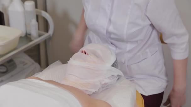 Professionele cosmetoloog vrouw verwijdert verband van het gezicht van een klant. — Stockvideo