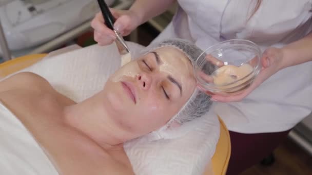 Profesjonalna kosmetolog kobieta zakłada maskę na twarz pacjenta. — Wideo stockowe