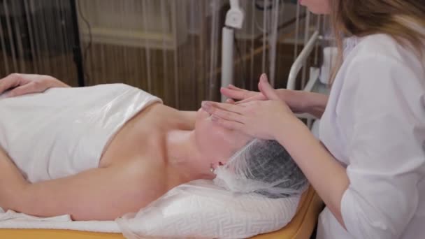 Donna cosmetologa professionista che fa il massaggio facciale a cliente di salone di bellezza . — Video Stock