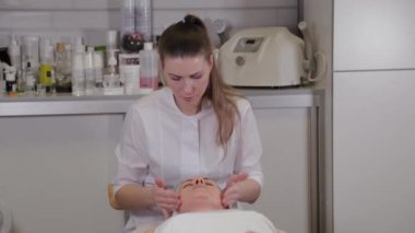Profesyonel kozmetik uzmanı kadın güzellik salonu müşterisine yüz masajı yapıyor..