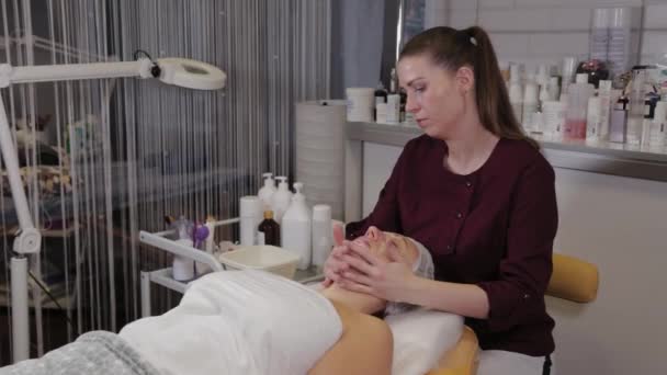 Una esteticista profesional lava la cara de los pacientes con jabón líquido y simultáneamente masajes . — Vídeos de Stock