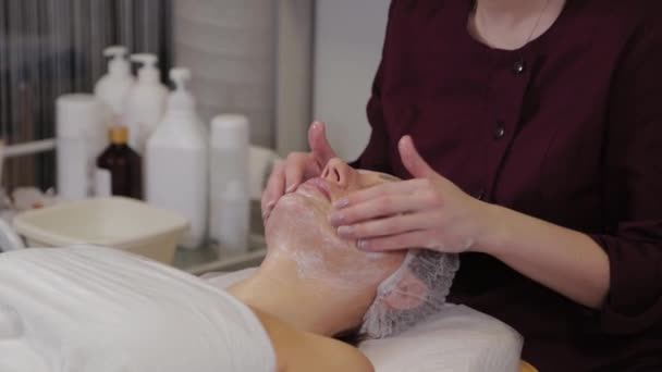Eine professionelle Kosmetikerin wäscht das Gesicht der Patientinnen mit Flüssigseife und massiert gleichzeitig. — Stockvideo