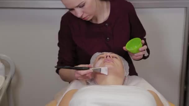 Donna cosmetologa professionista mette una maschera sul viso del paziente . — Video Stock