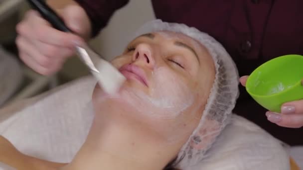 Donna cosmetologa professionista mette una maschera sul viso del paziente . — Video Stock