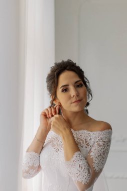 Güzel gelin pencerenin kenarına küpe takar. Mutlu düğün günleri..