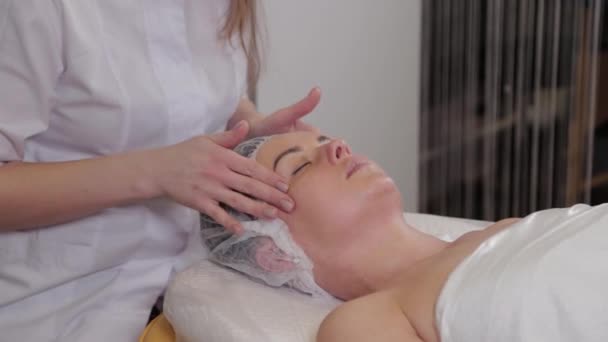 Cosmetologist profissional mulher fazendo massagem facial ao cliente de salão de beleza . — Vídeo de Stock