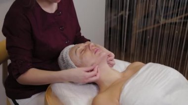 Profesyonel kozmetik uzmanı kadın güzellik salonu müşterisine yüz masajı yapıyor..